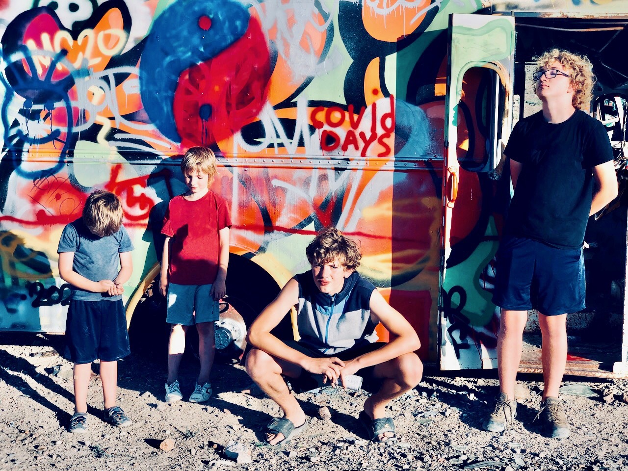 Four kids in front of a spray-painted bus with "COVID Days" written on the bus.